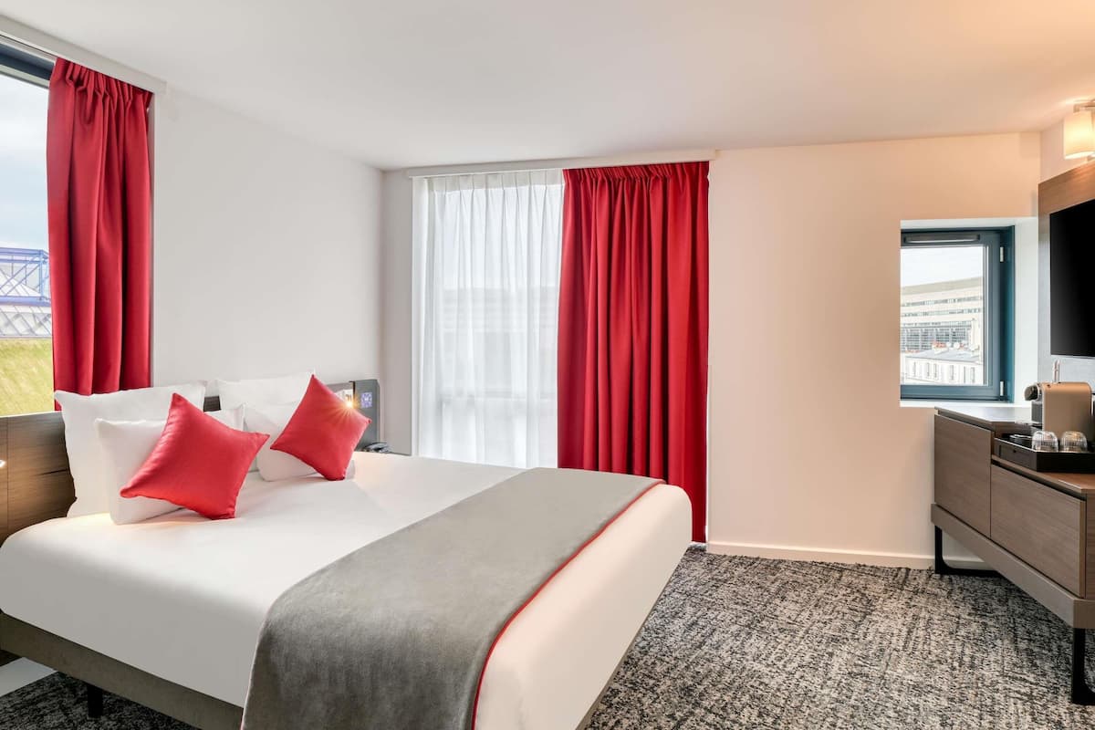 A hotel room with a bed, a desk, a chair, a TV, and a window with curtains.