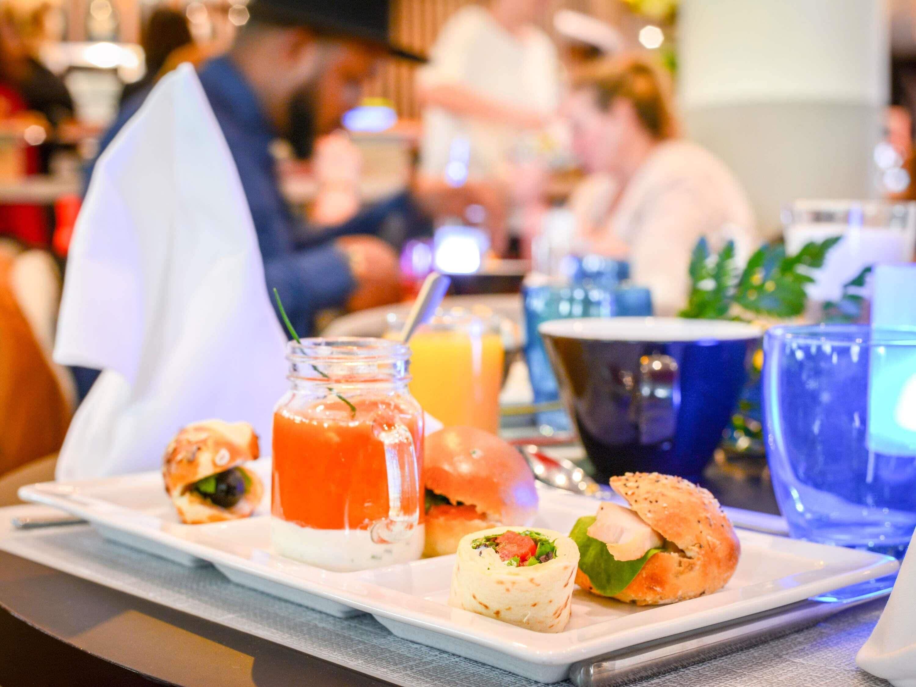 A dining table with a variety of food items including a sandwich, a wrap, and a drink in a jar.