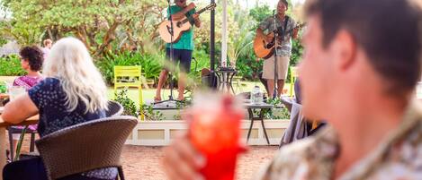 Un patio al aire libre con escenario para música en vivo, disposición de asientos y zona de comedor informal.