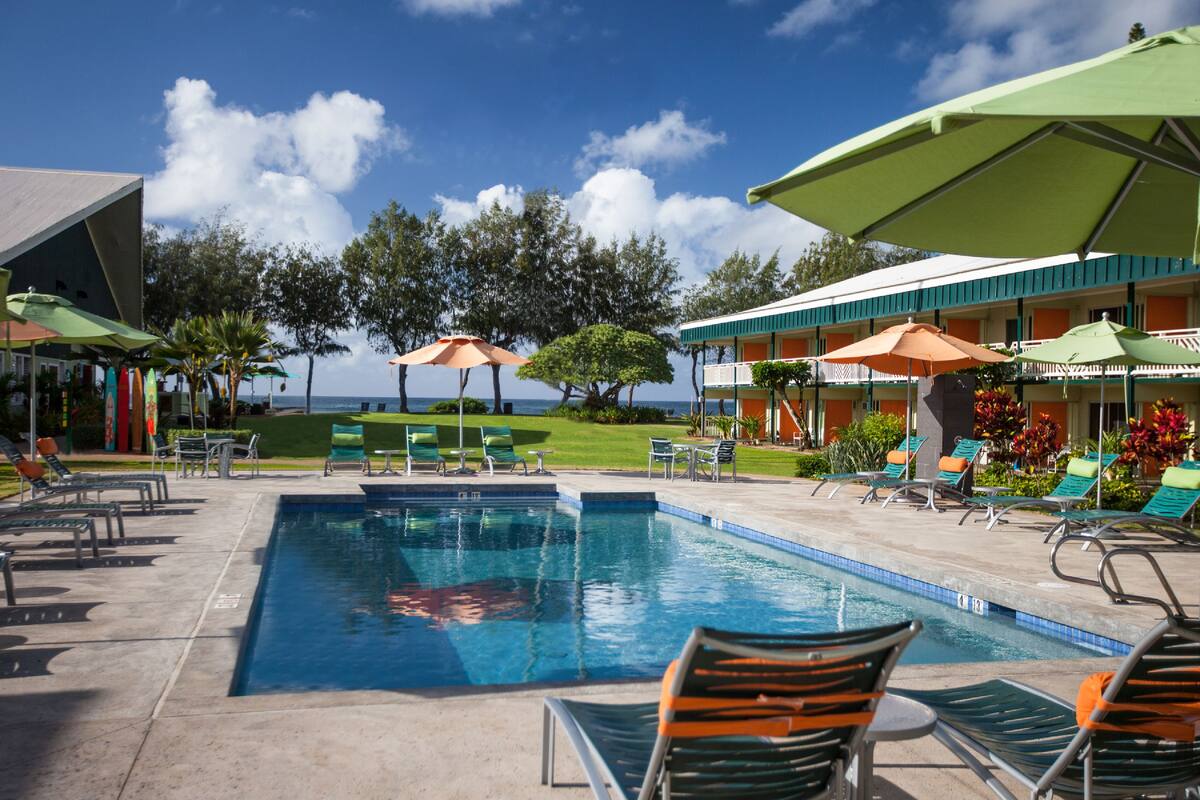 A pool area with lounge chairs and umbrellas, a view of the ocean, and a building with a balcony.