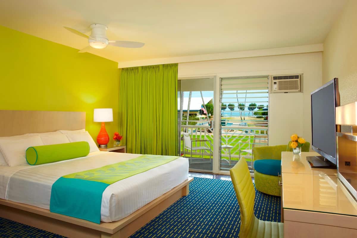 Habitación de hotel con cama, escritorio, televisión, balcón con vistas y ventilador de techo.