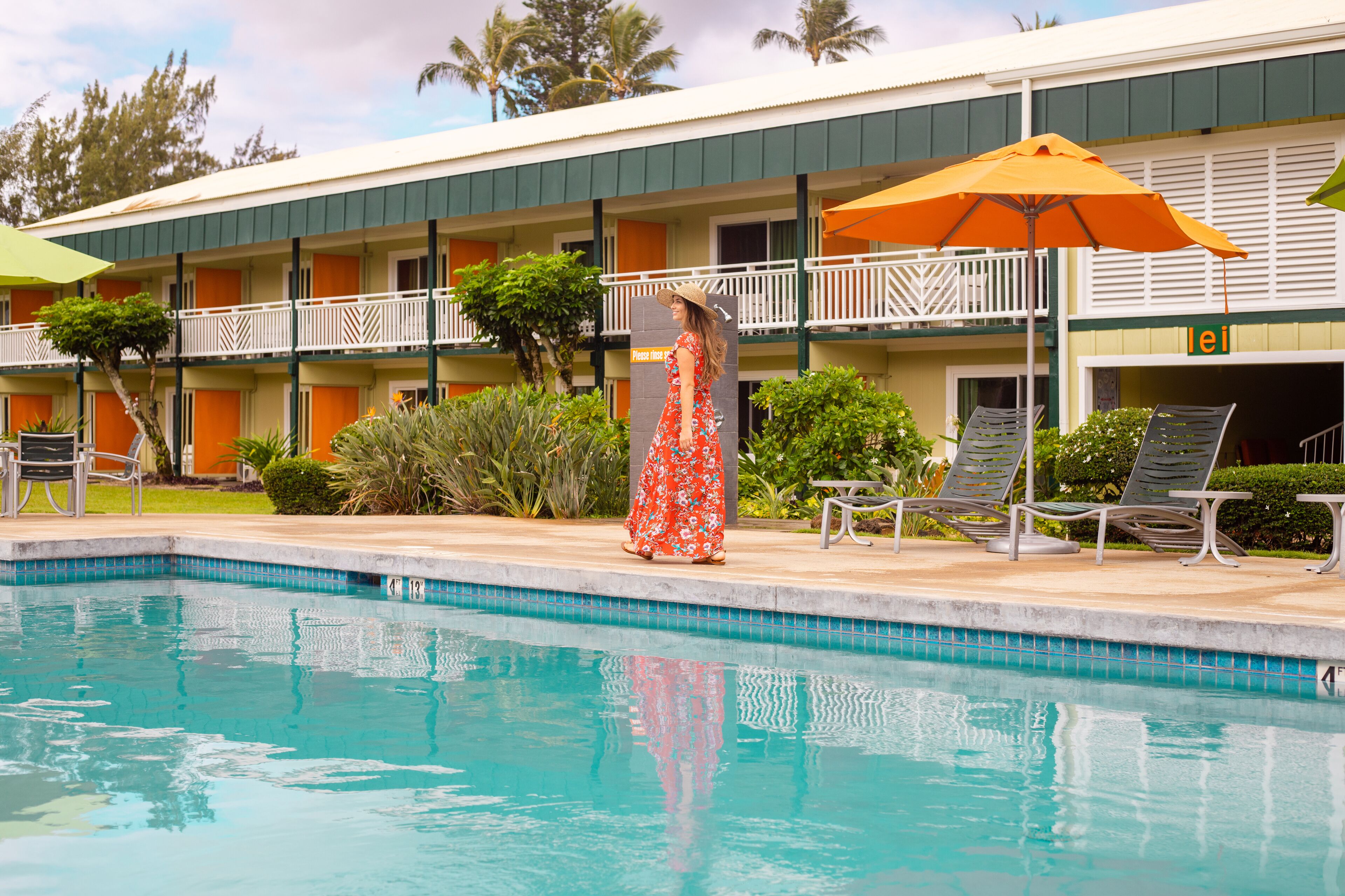 Et hotel med swimmingpool, udendørs siddepladser og et skilt, der står 'Vent venligst'.