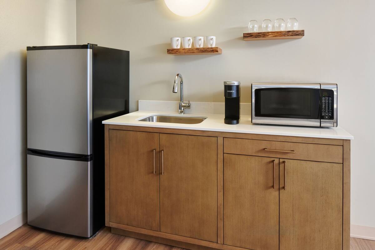 A kitchen with a stainless steel refrigerator, a microwave, a coffee maker, and wooden cabinets.