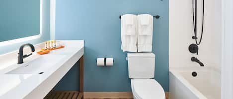 Een badkamer met een witte wastafel, toilet en bad. Twee handdoeken hangen aan de muur.
