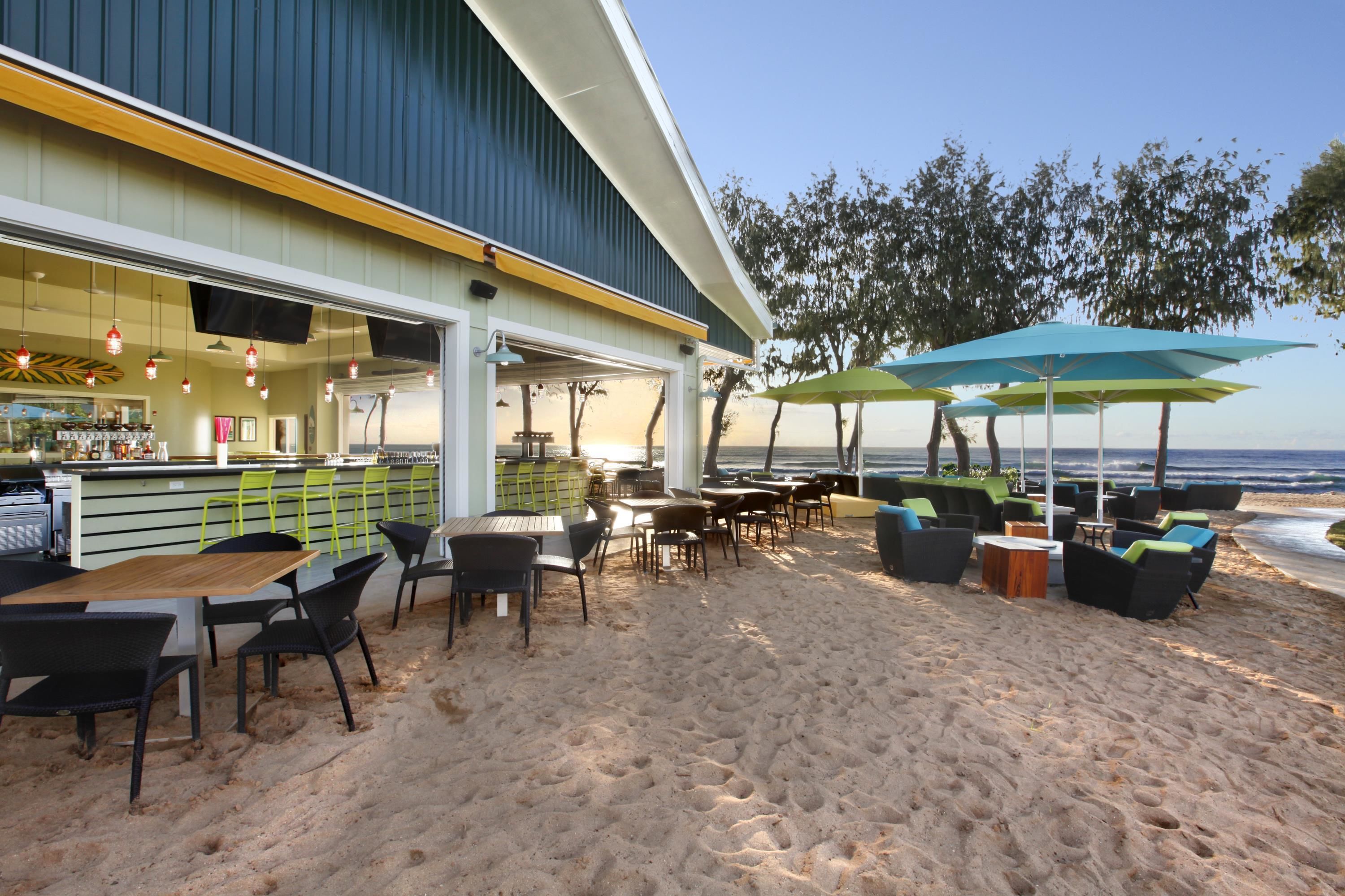 A beachfront restaurant with outdoor seating, a bar, and a view of the ocean.