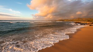 A beach with waves, a clear sky, and distant hills. - Kauai Shores Hotel (Kapaa)