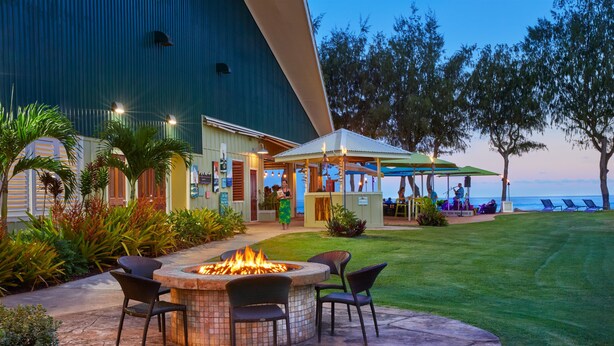 A patio with a fire pit and chairs, a covered seating area with umbrellas, and a view of the ocean. - Kauai Shores Hotel (Kapaa)