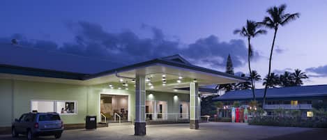 A hotel with a covered entrance, a car parked in front, and palm trees in the background.