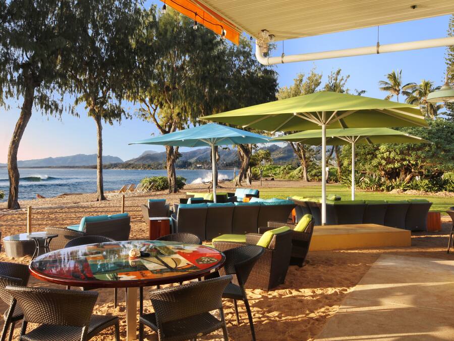 An outdoor seating area with tables and chairs, umbrellas, and a view of the ocean.