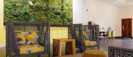 Eine Empfangshalle mit Korbmöbeln, einem Holztisch und einer grünen Wand mit dem Schriftzug "Kauai Shores Hotel".