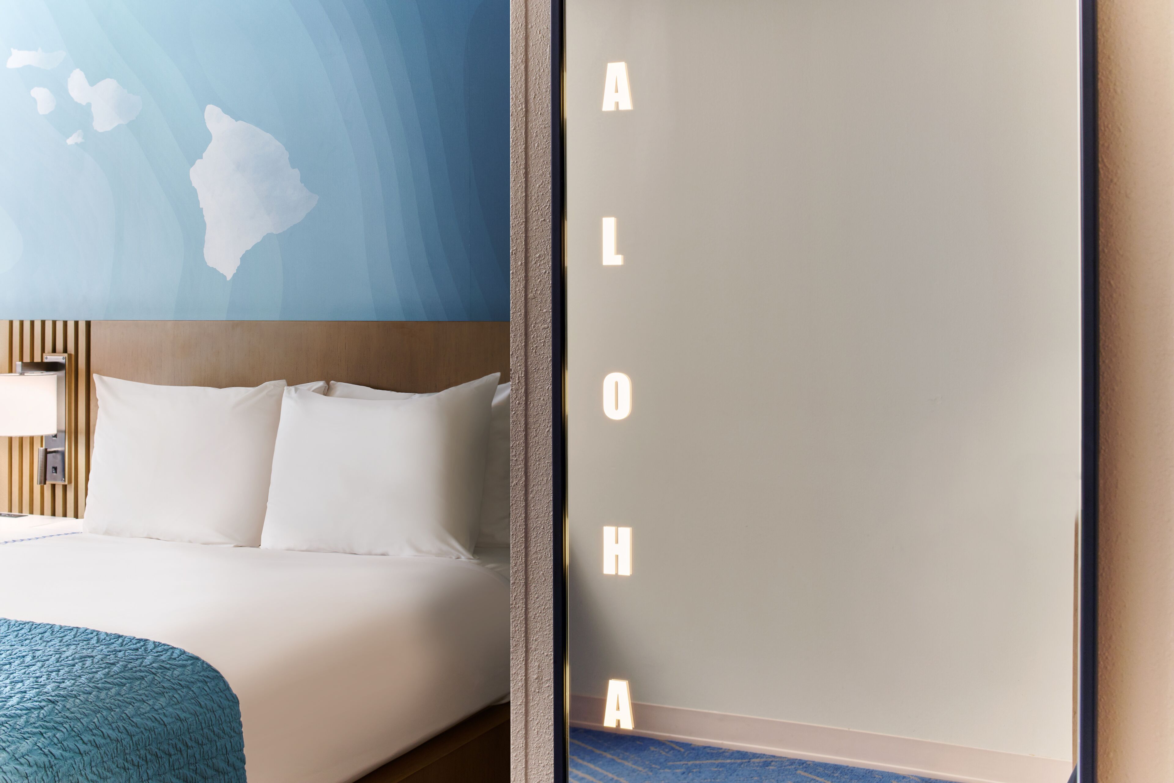Una habitación de hotel con una cama, un mapa en la pared y una pared con letras iluminadas que deletrean "ALOHA".