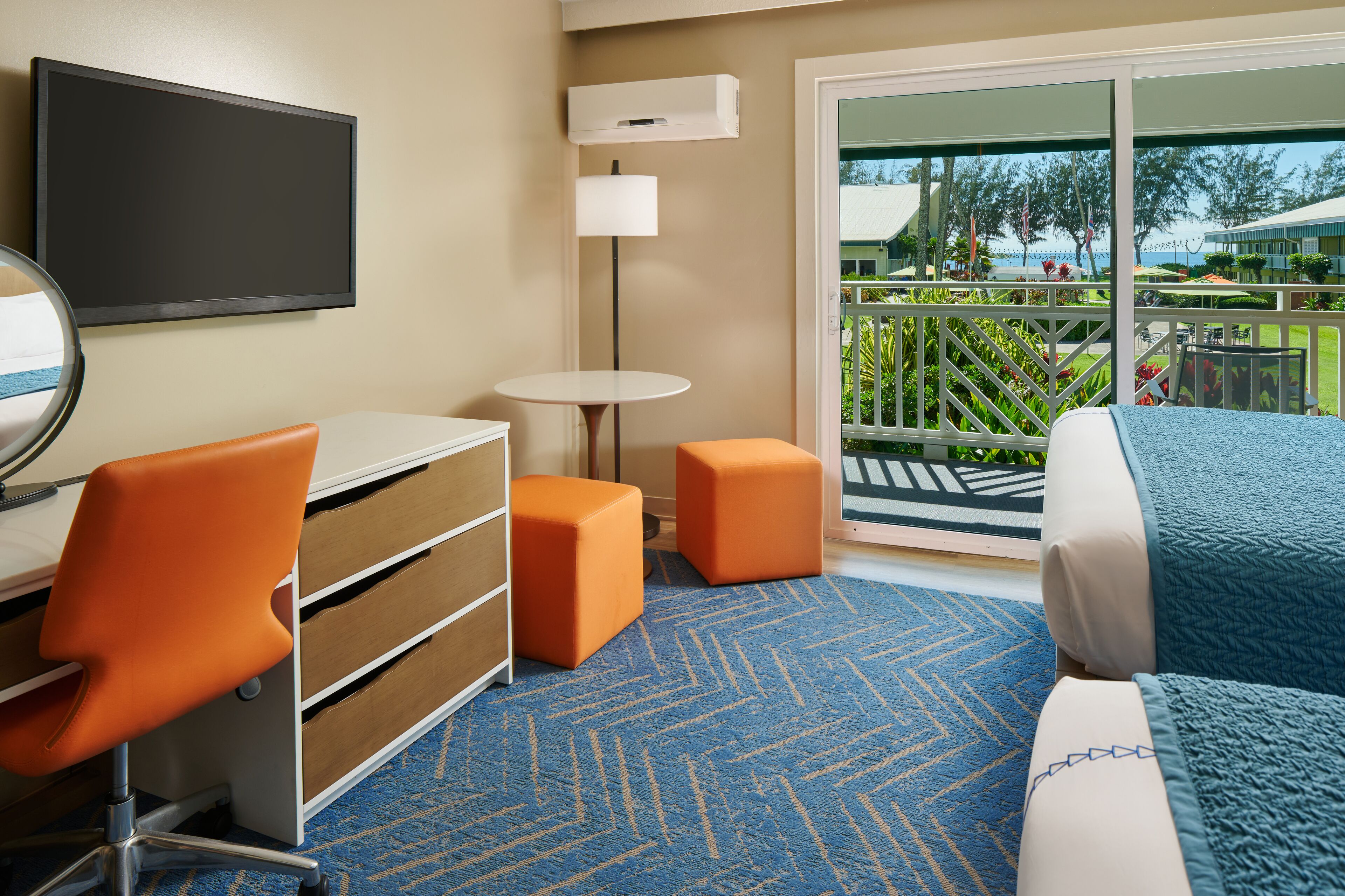 A hotel room with a bed, a desk with a chair, a small table, and a large window with a view of the outdoors.