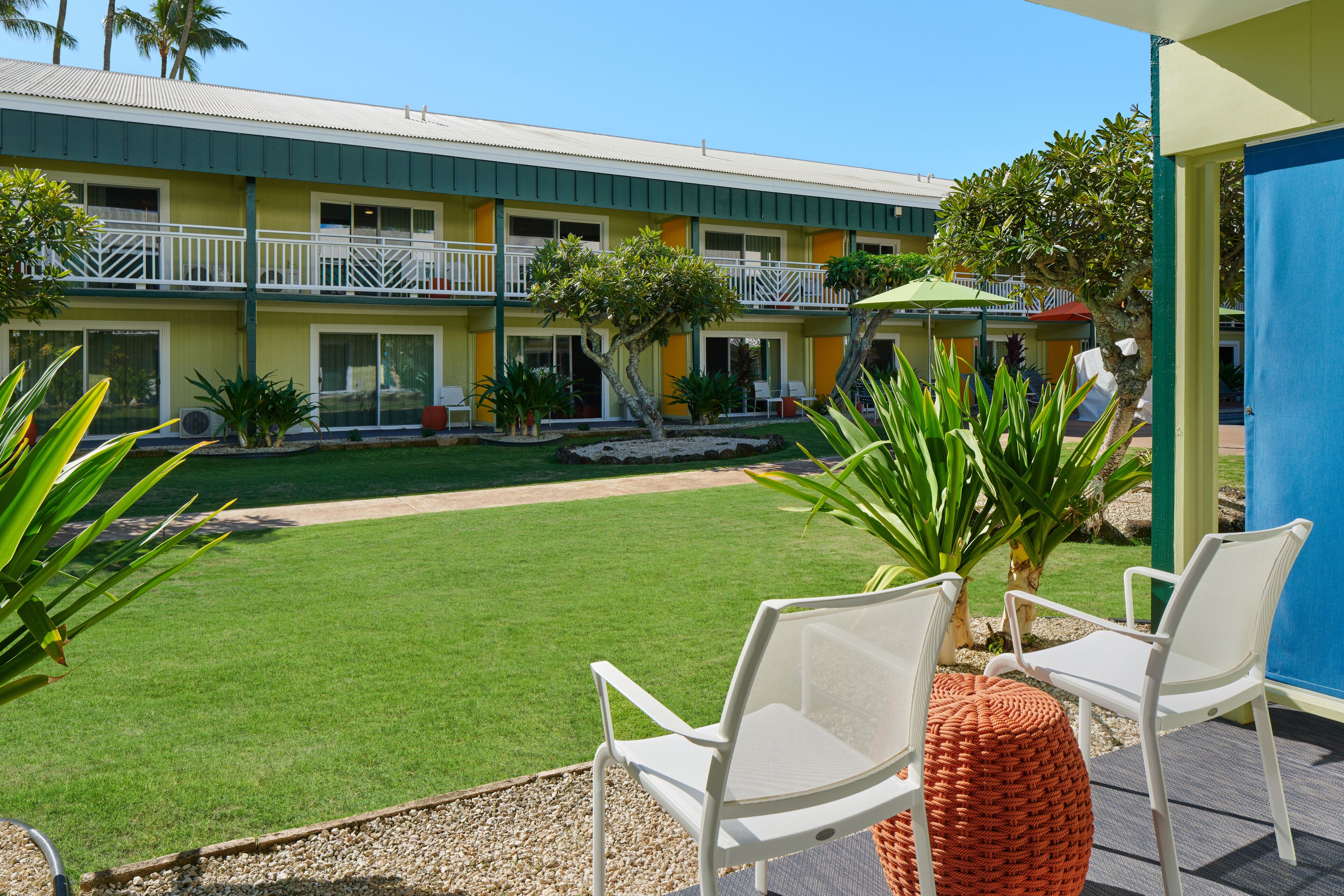 A hotel with a green lawn, white chairs, and a blue door.