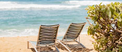 Two beach chairs on a sandy beach with the ocean in the background.