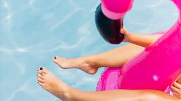 Une personne se détend sur un matelas gonflable rose dans une piscine à l’eau cristalline.