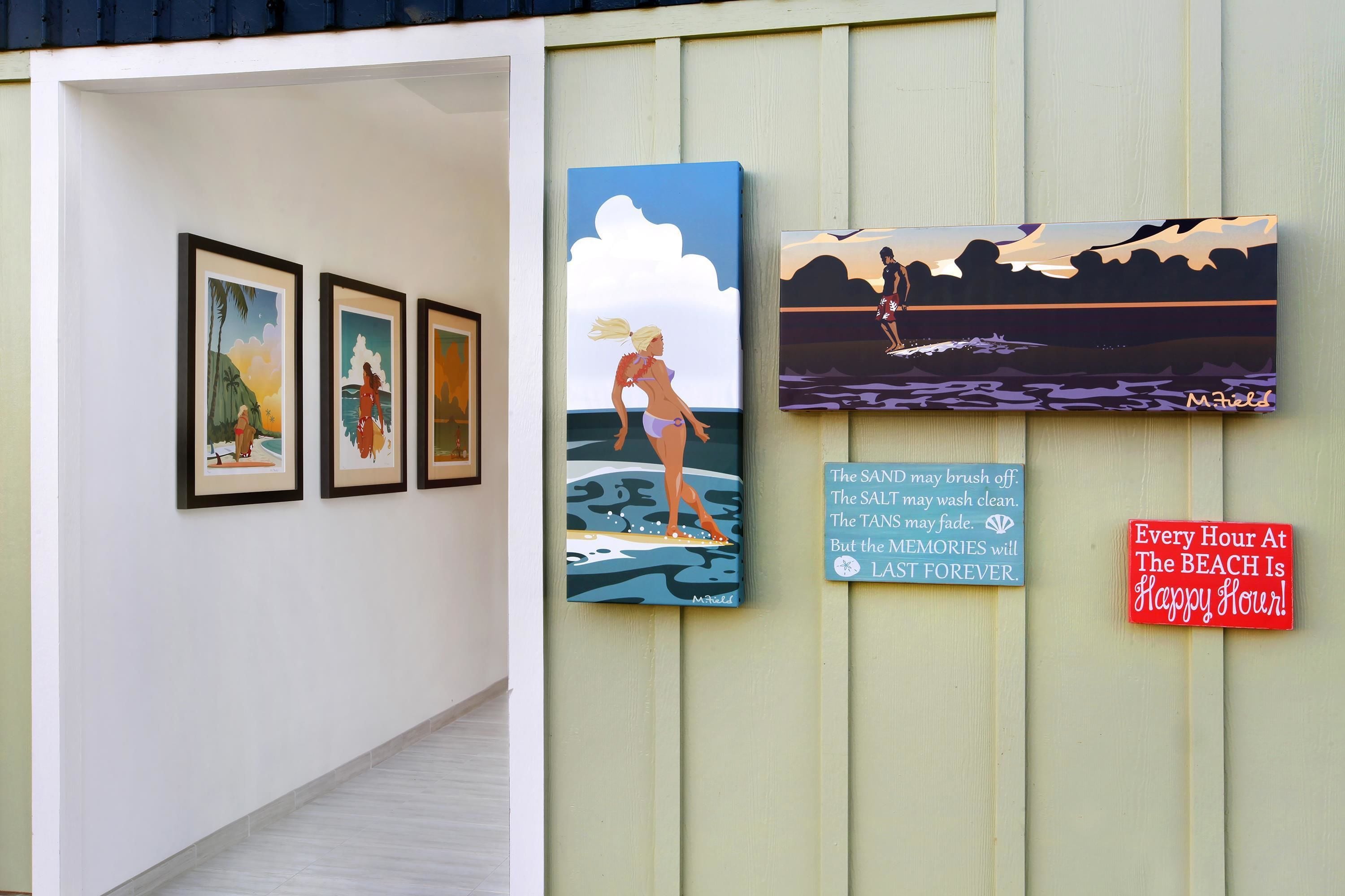 A hallway with framed artworks and a sign that reads "Every Hour At The Beach Is Happy Hour!"