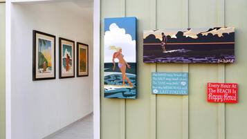 A hallway with framed artworks and a sign that reads "Every Hour At The Beach Is Happy Hour!"