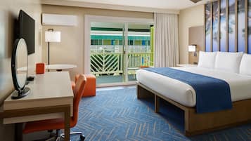 Quarto de hotel com cama, escrivaninha com cadeira, mesa pequena, espelho e varanda com vista para palmeiras.