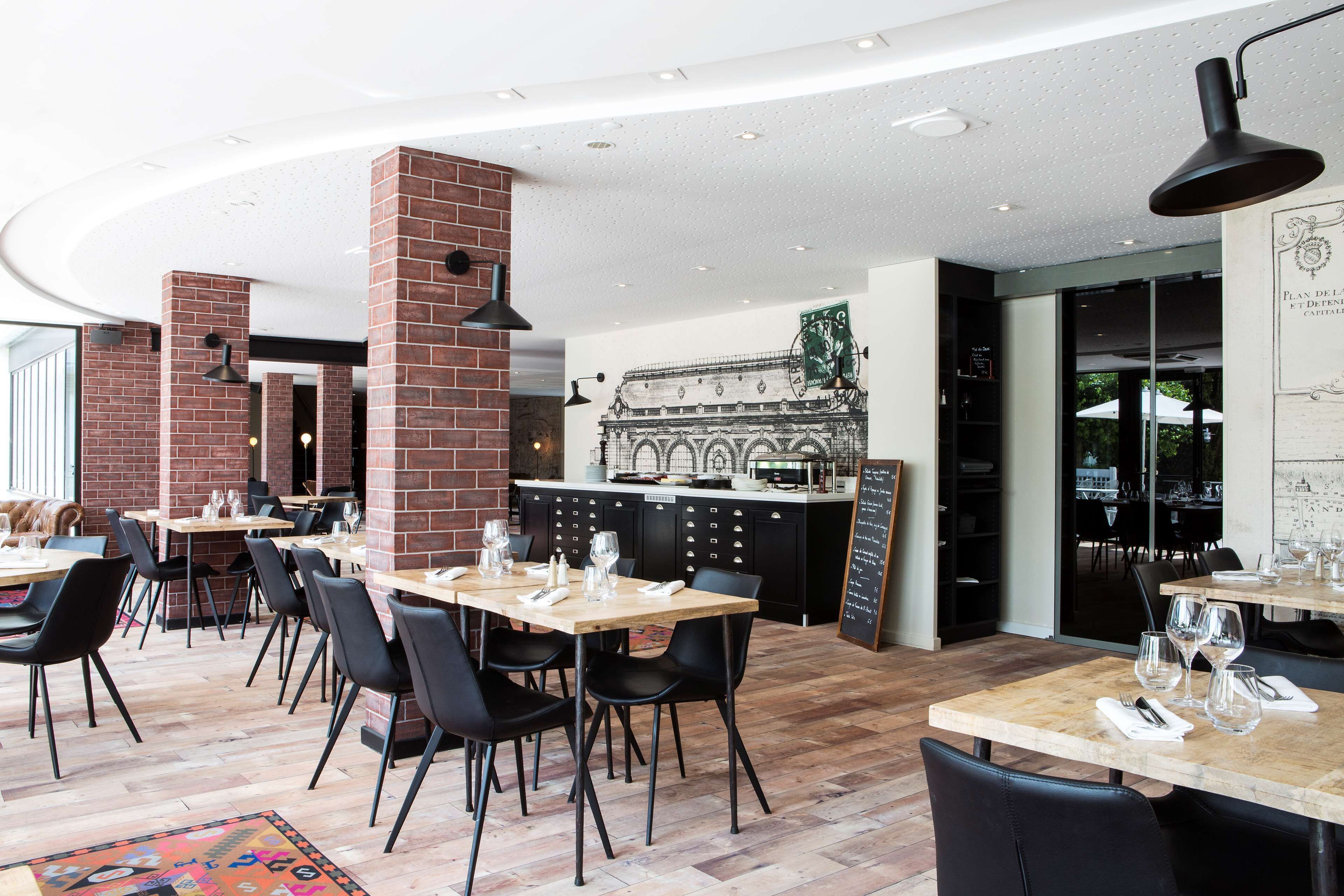 A modern restaurant with brick walls, wooden tables, and black chairs.