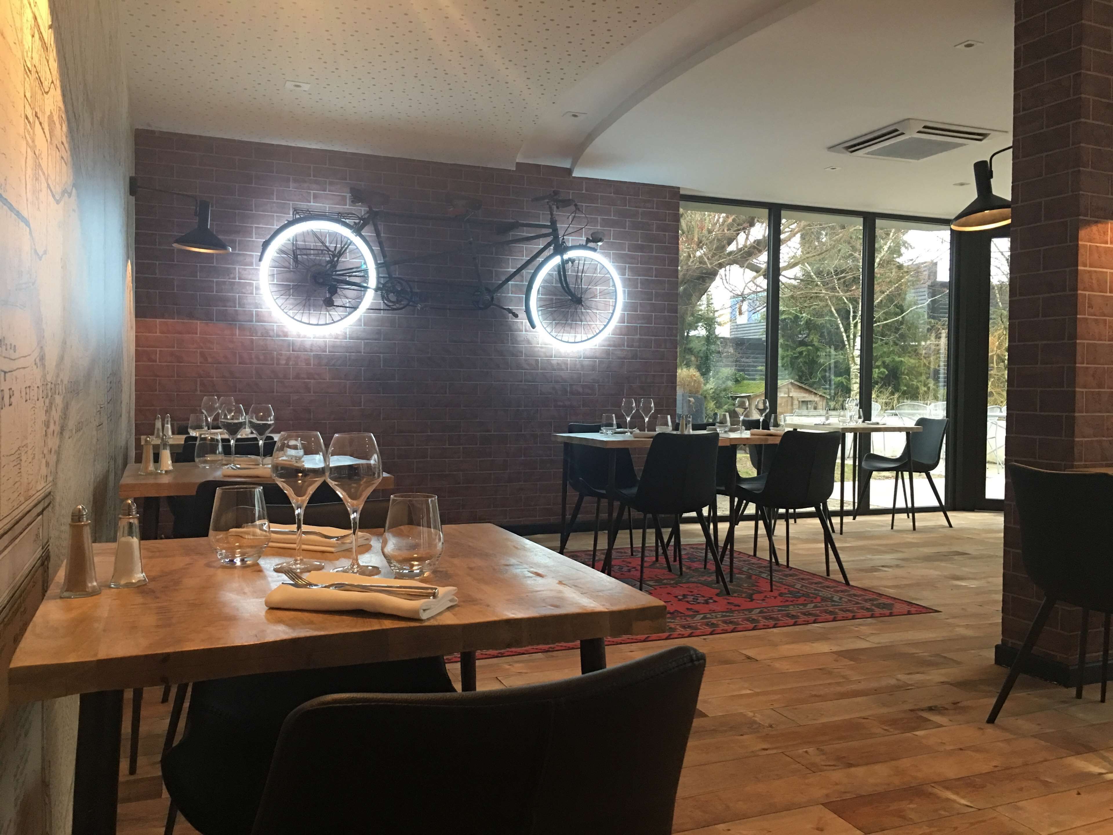 Un interior de restaurante con paredes de ladrillo, lámparas de mesa redondas y vistas amplias a través de ventanas grandes.