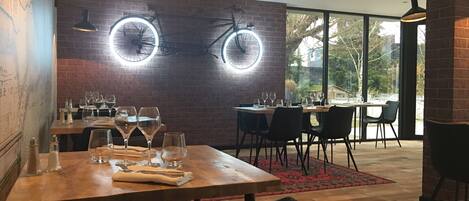 Un interior de restaurante con paredes de ladrillo, lámparas de mesa redondas y vistas amplias a través de ventanas grandes.