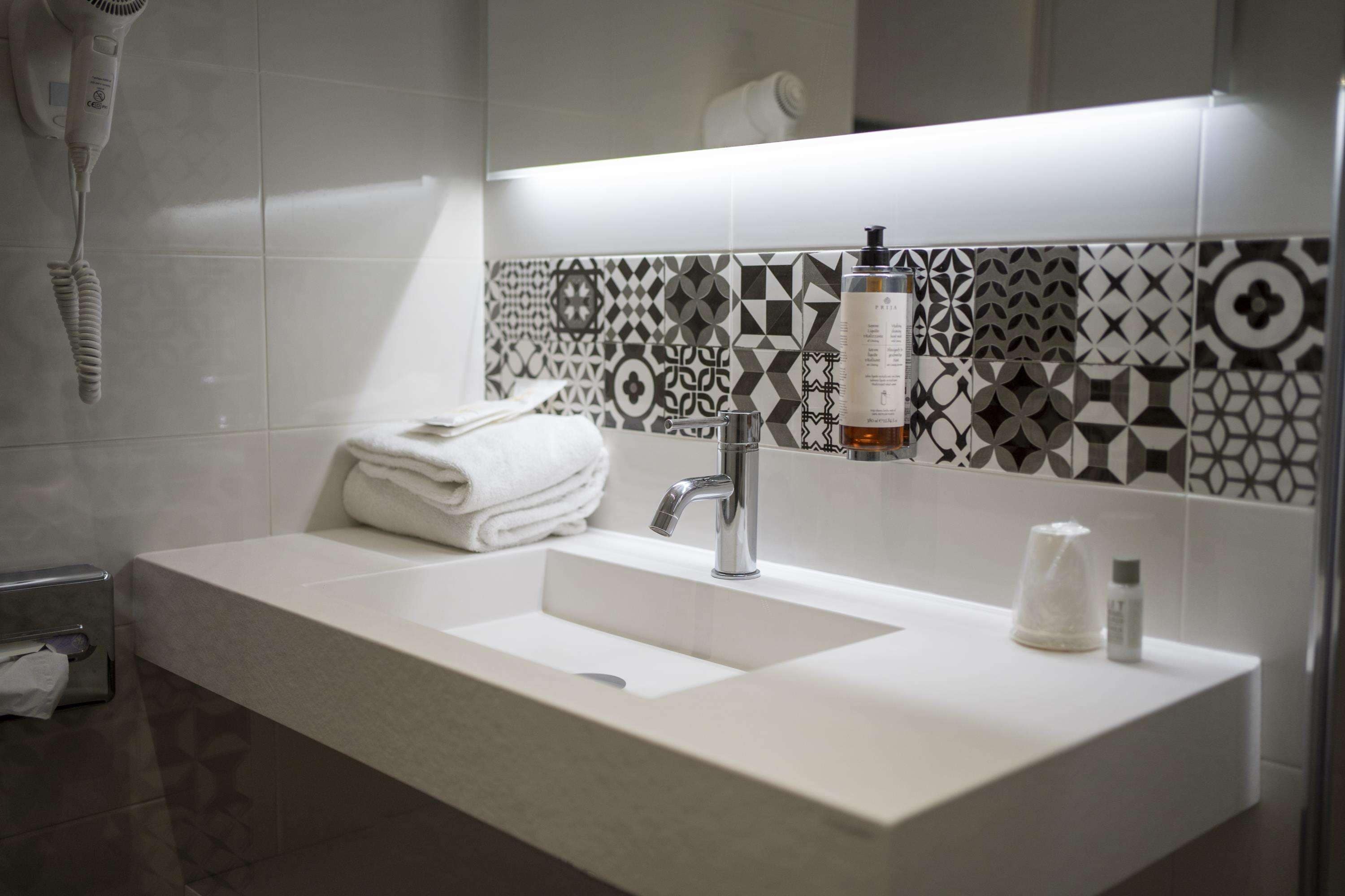 Een moderne badkamer met een witte wasbak, een spiegel en betegelde vloeren.