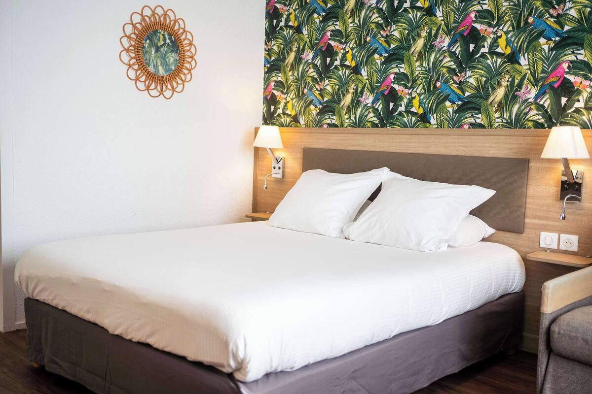Cama bem arrumada com lençóis brancos, cabeceira de madeira e duas luminárias laterais.