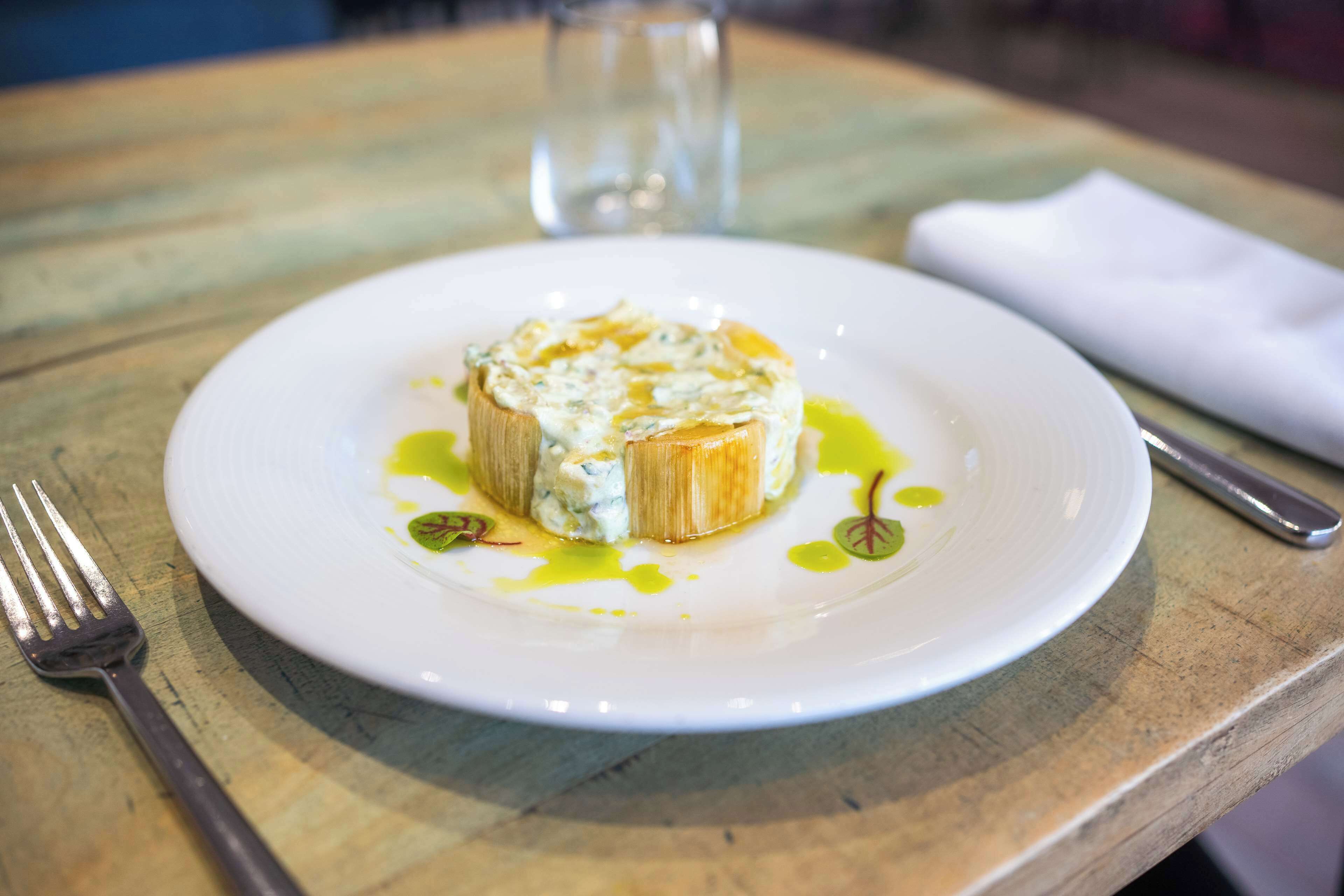 A plate with a food item on a wooden table, a fork, and a napkin.