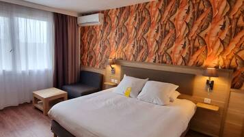 A hotel room with a large bed, two bedside tables, a nightstand, a wall-mounted air conditioner, and a window with curtains.