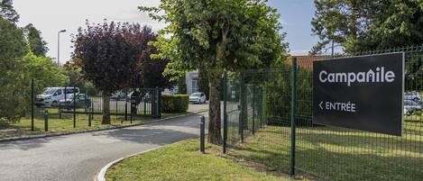 A sign for Campanile with a curved road leading to it, surrounded by greenery and a fence.