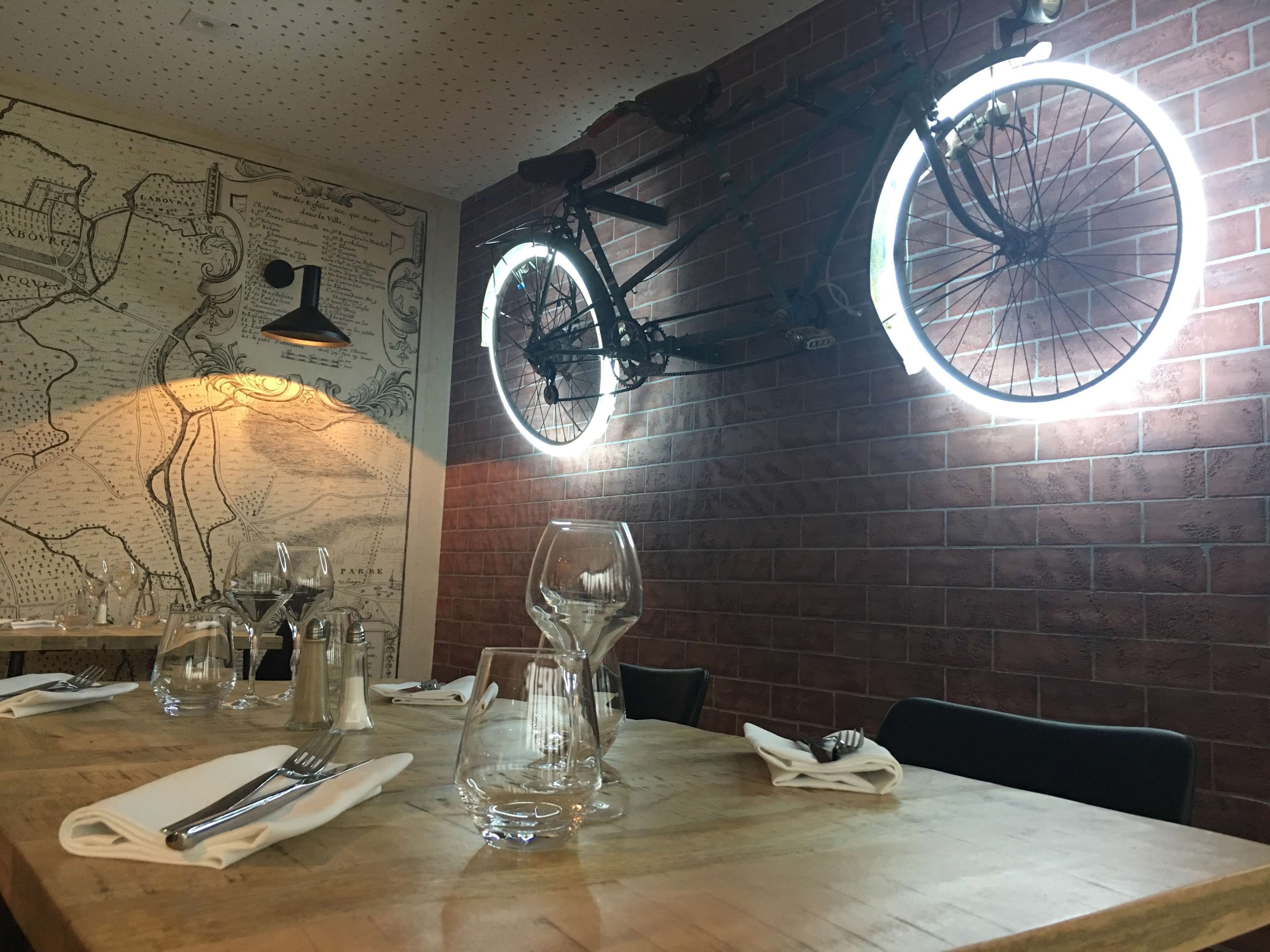 A restaurant interior with a wooden table set for dining, a bicycle mounted on the wall, and a map on the wall.