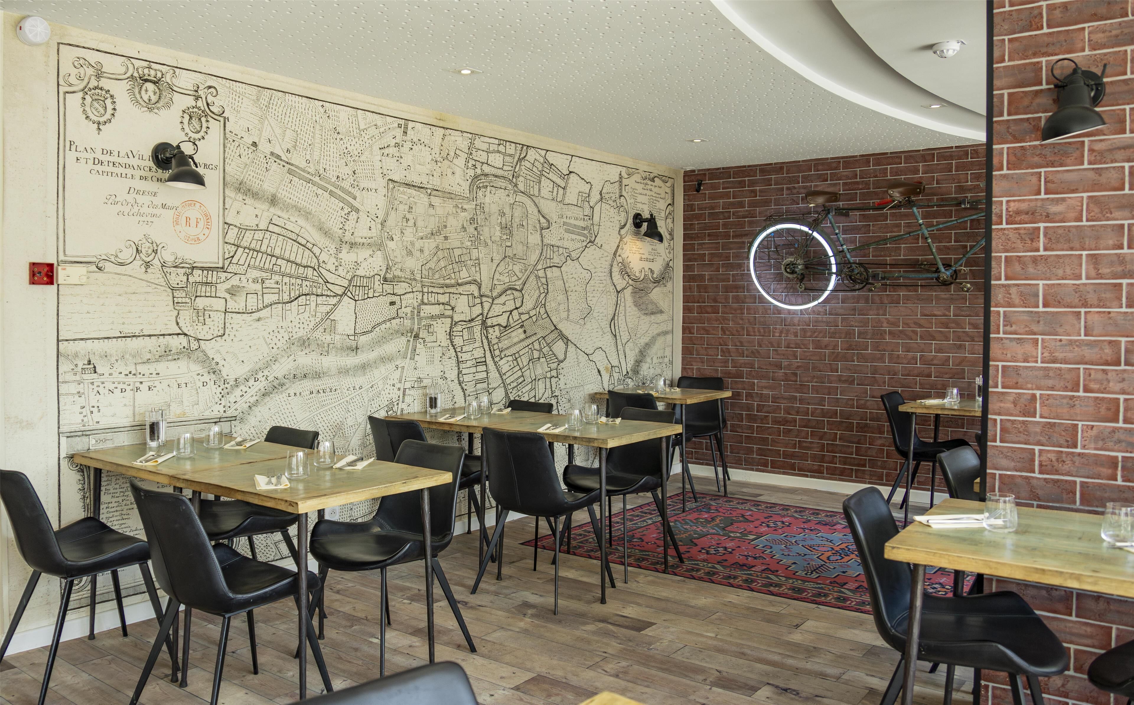Restaurante com um grande mapa antigo na parede, mesas de madeira, cadeiras pretas e uma parede de tijolos com uma bicicleta pendurada.