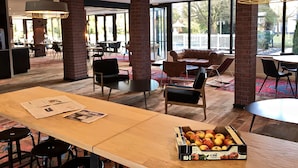 A modern dining area with brick pillars, large windows, and a variety of seating options including tables and chairs. - Campanile PRIME - Troyes Nord Barberey (Barberey-Saint-Sulpice)