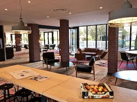 Un comedor moderno con pilares de ladrillo, ventanas amplias y diversas opciones de asiento, incluyendo mesas y sillas.