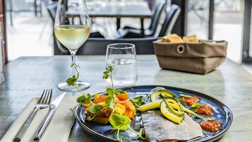 A dining table with a plate of food, a glass of white wine, and a water glass.