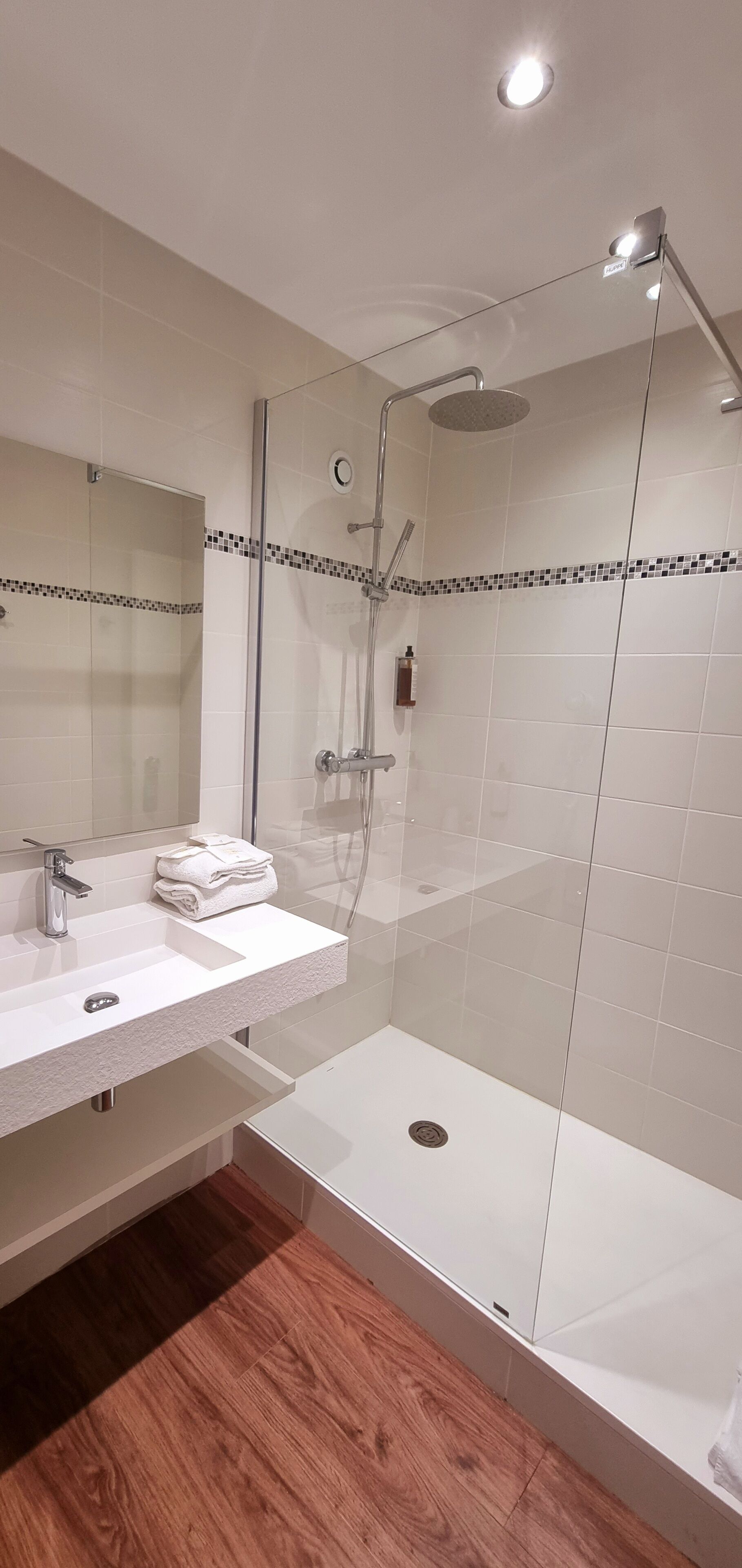 A modern bathroom with a glass-enclosed shower, a white sink with a mirror, and a tiled floor.