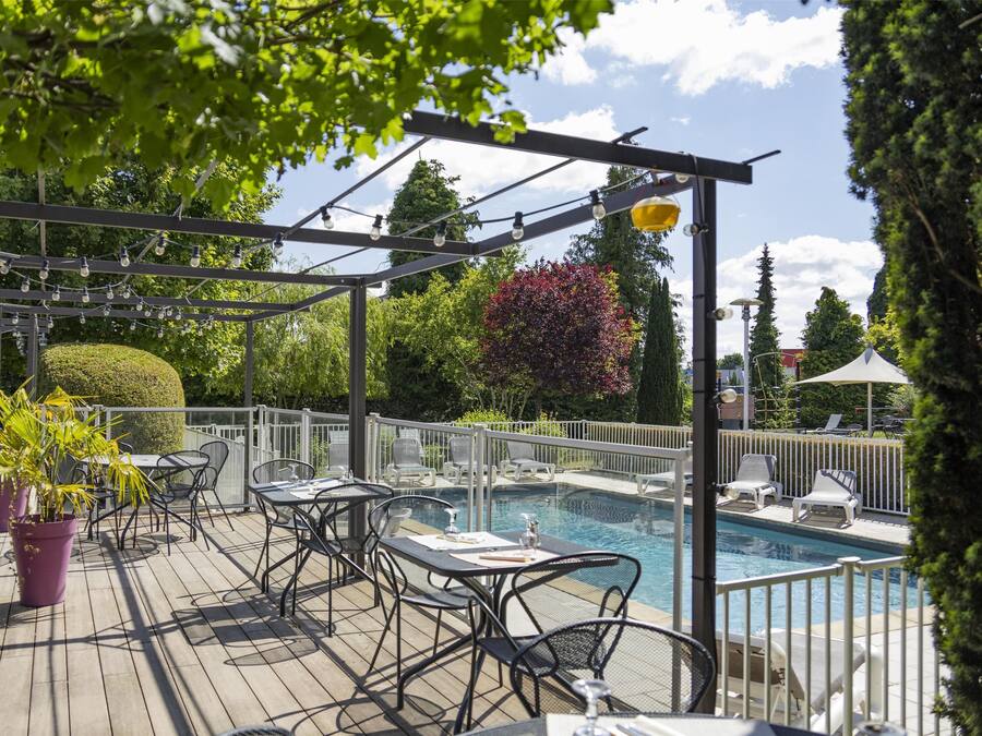 Ein Poolbereich im Freien mit einer Pergola, Sitzgelegenheiten und Kübelpflanzen.