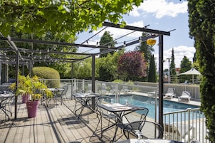 Un área de piscina al aire libre con una pérgola, asientos y plantas en macetas.