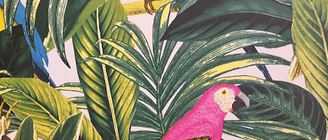 A vibrant tropical scene with two colorful parrots perched among lush green leaves and pink flowers.