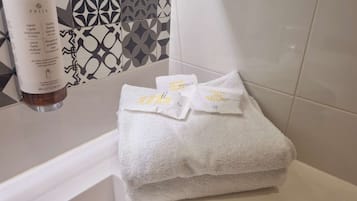 Un baño con una toalla blanca sobre un lavamanos, una botella de crema para manos y una toalla con texto.