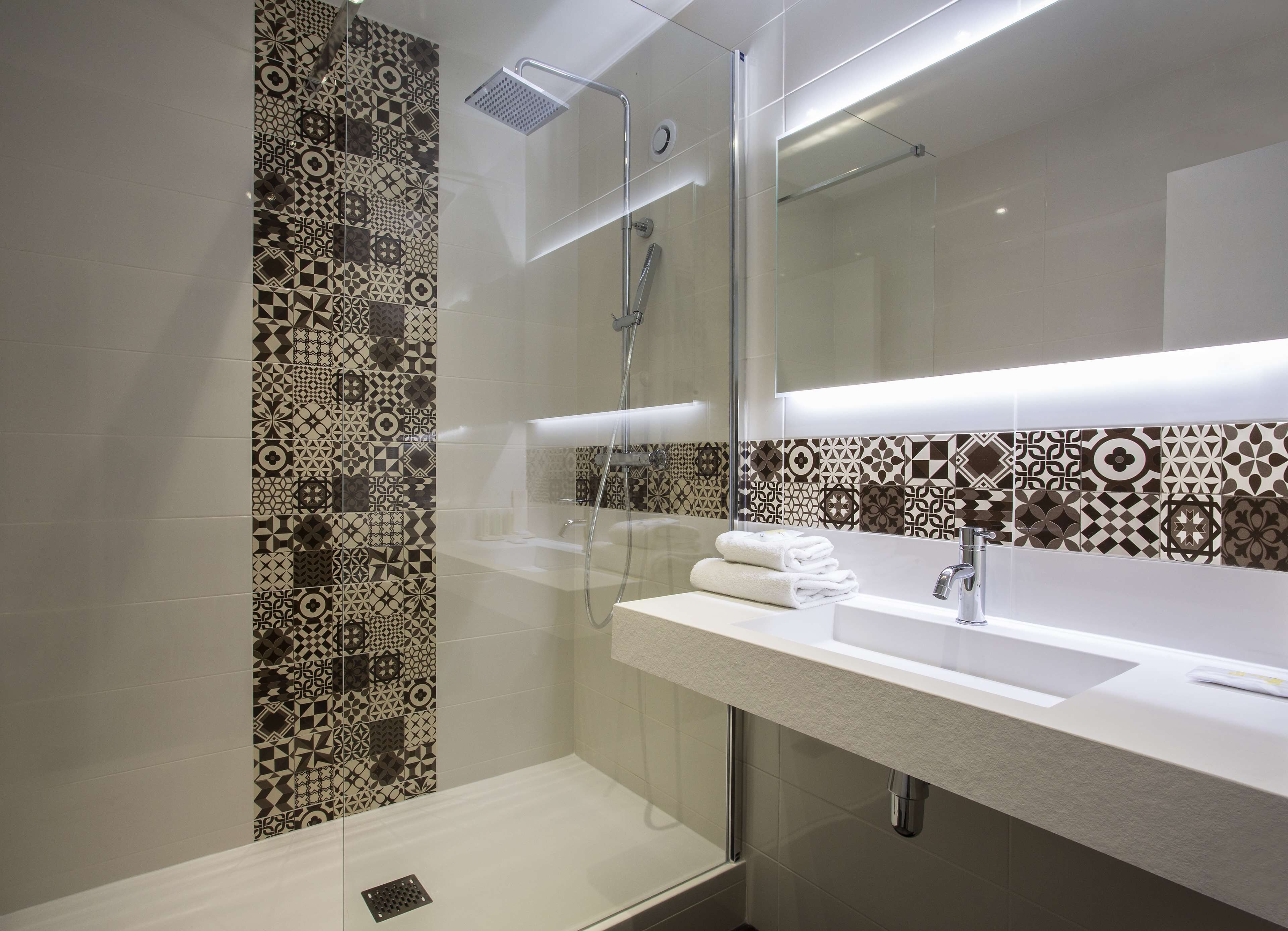 A modern bathroom with patterned tiles, a glass-enclosed shower, a white sink, and a mirror.