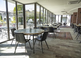 Un comedor moderno con mesas y sillas redondas, ventanas amplias que ofrecen vistas al exterior y una combinación de iluminación natural y artificial.