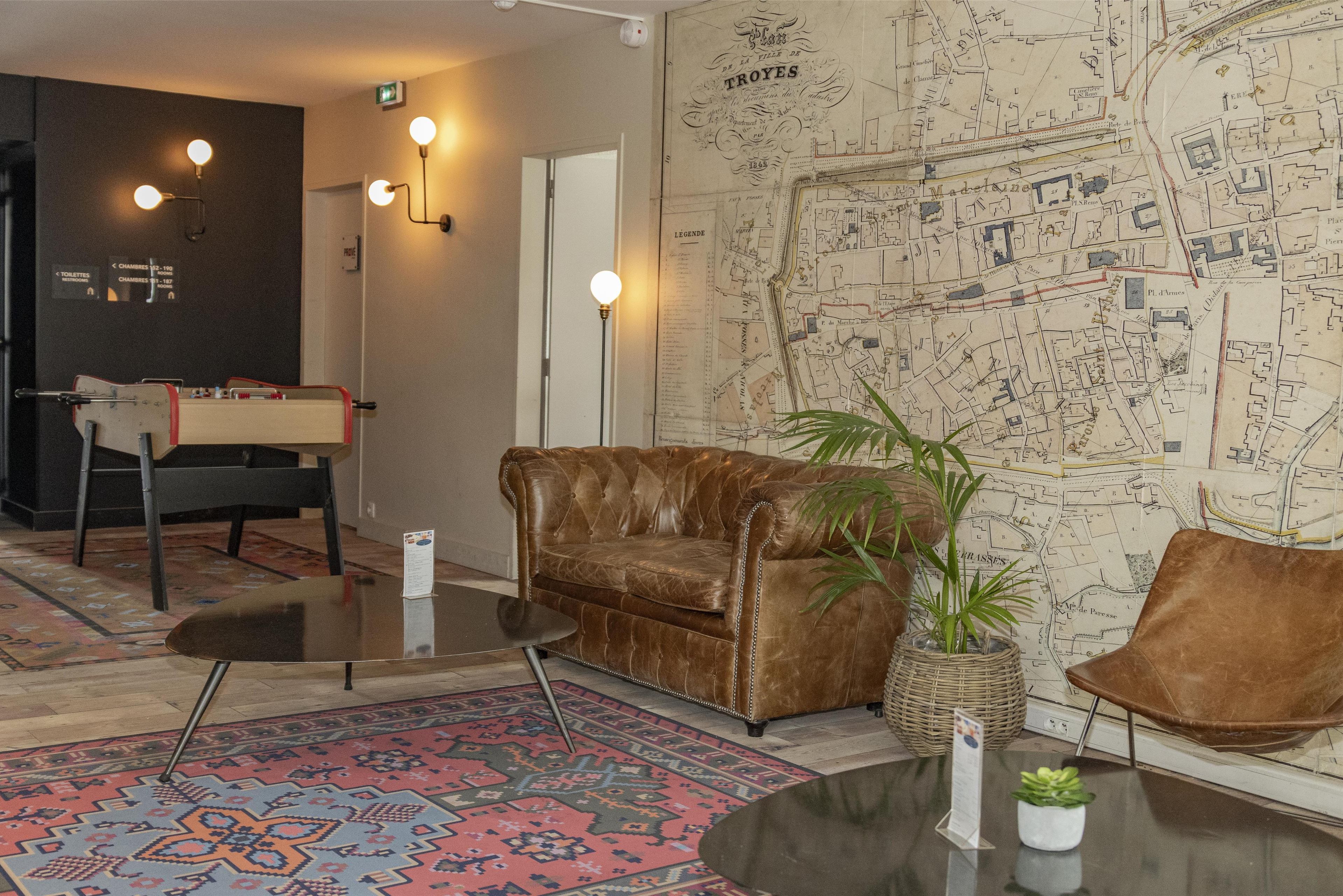 Une pièce avec un canapé en cuir marron, une petite table, une plante en pot et une carte accrochée au mur.