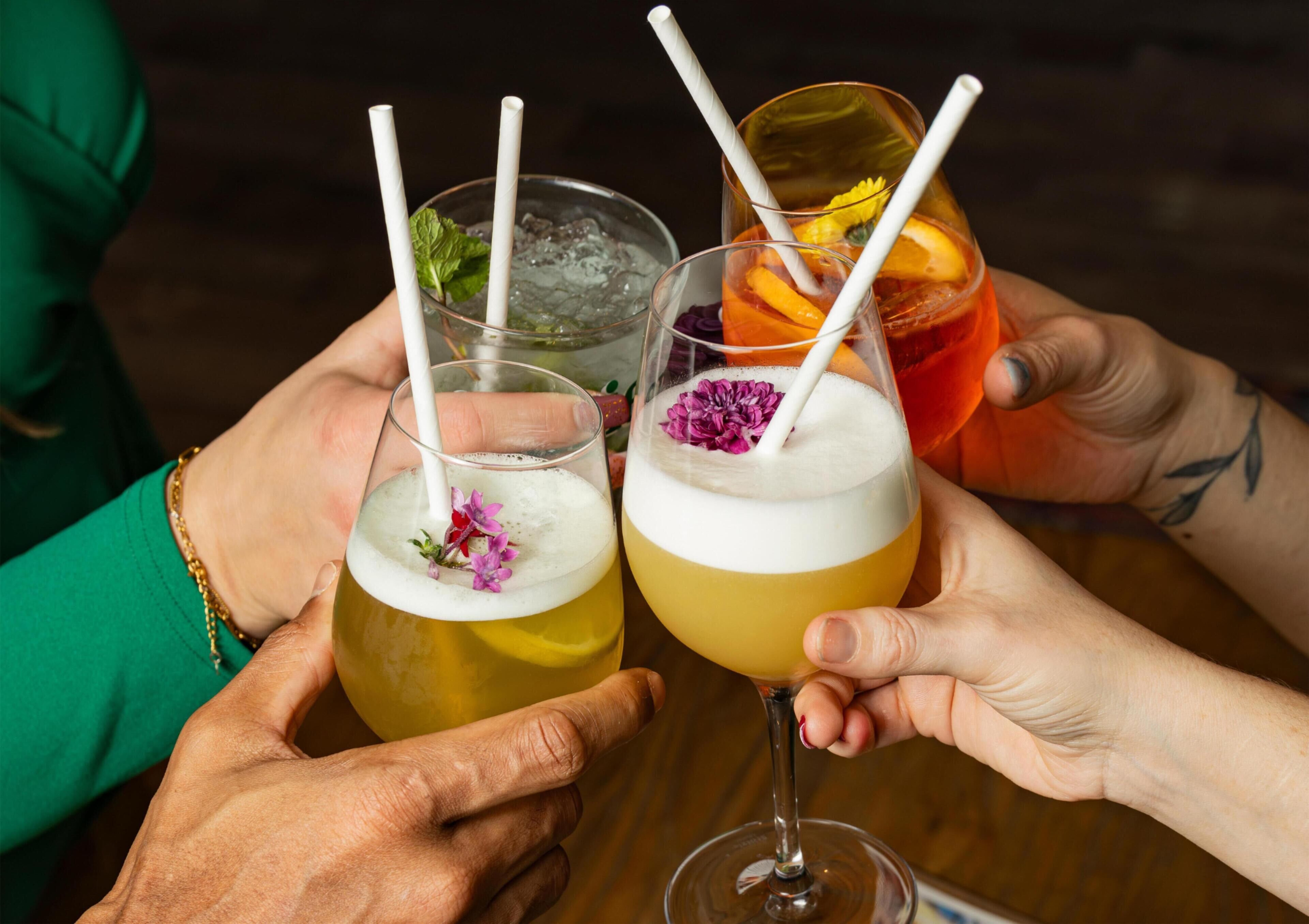 Two people holding glasses of cocktails with straws and garnishes.