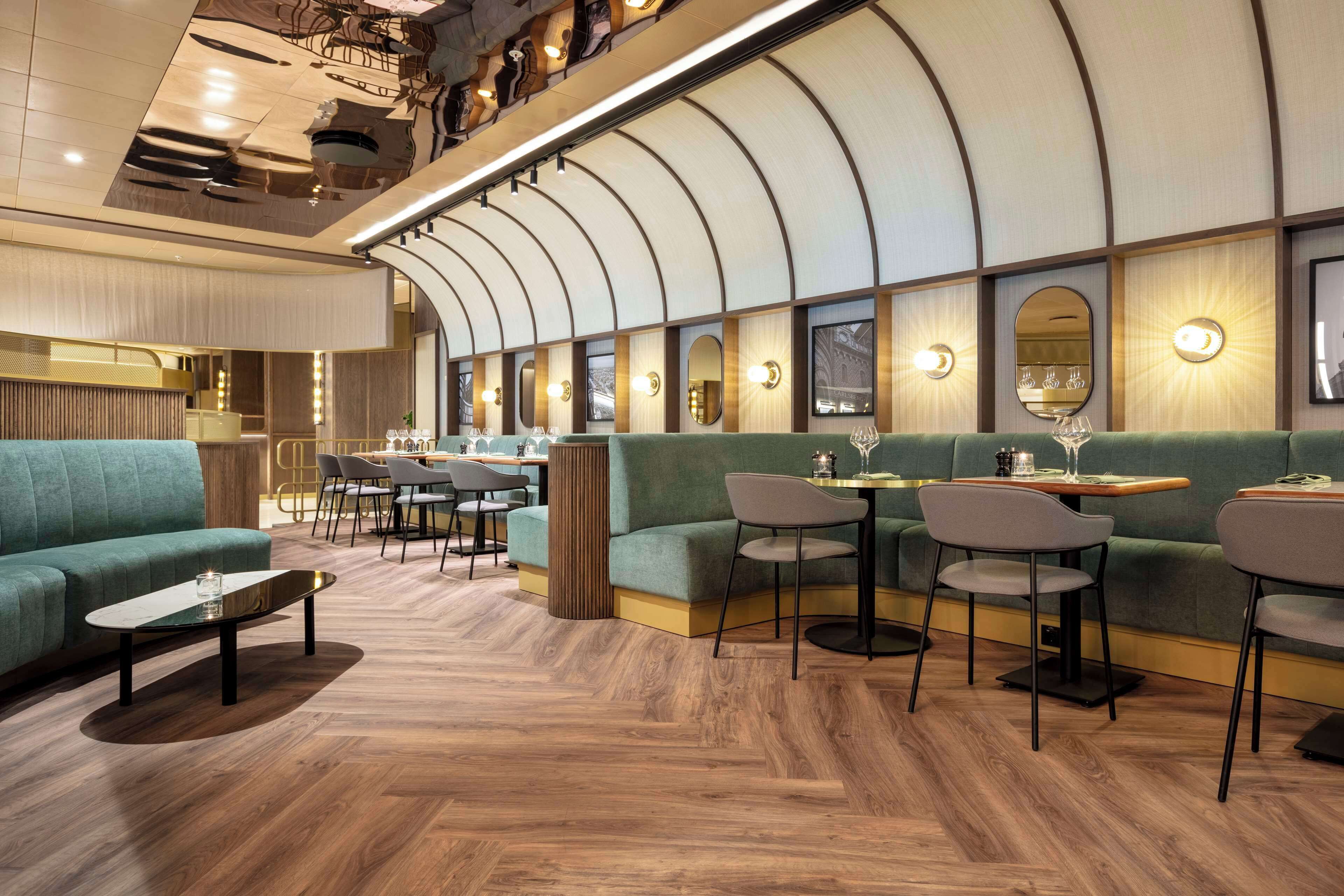 A modern restaurant with green seating, wooden flooring, and a curved ceiling design.