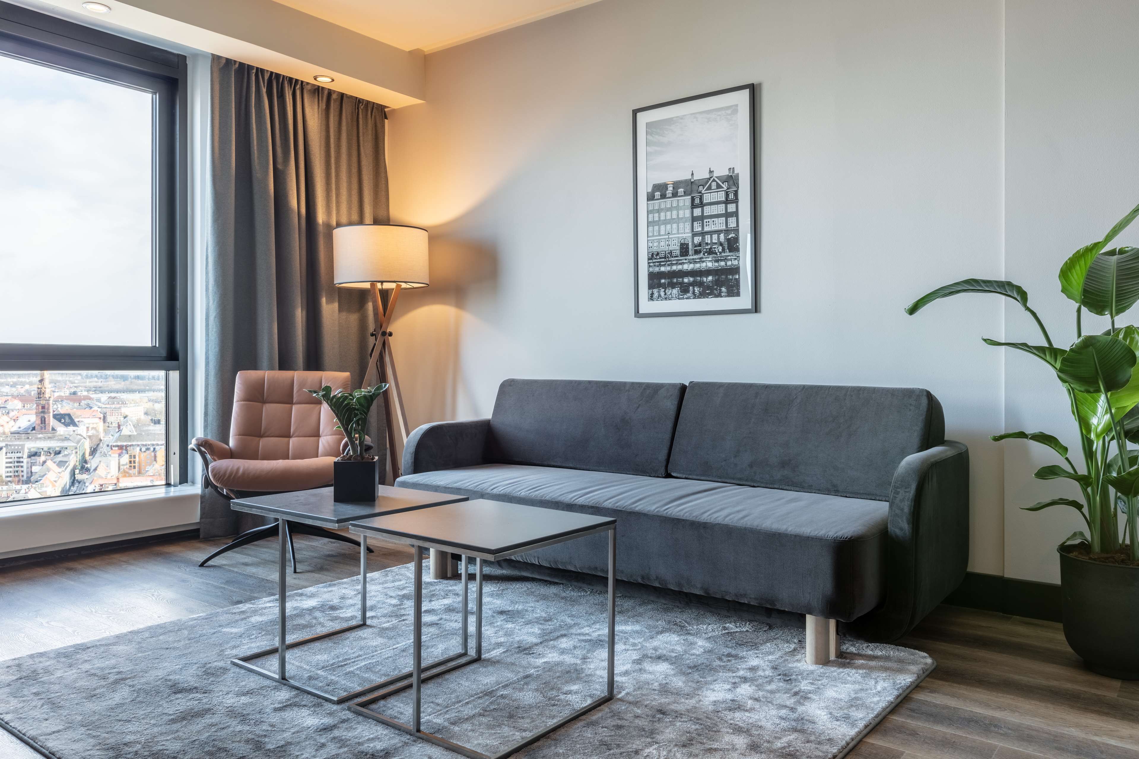En moderne stue med en grå sofa, en brun lænestol, et lille bord, en gulvlampe og en potteplante.