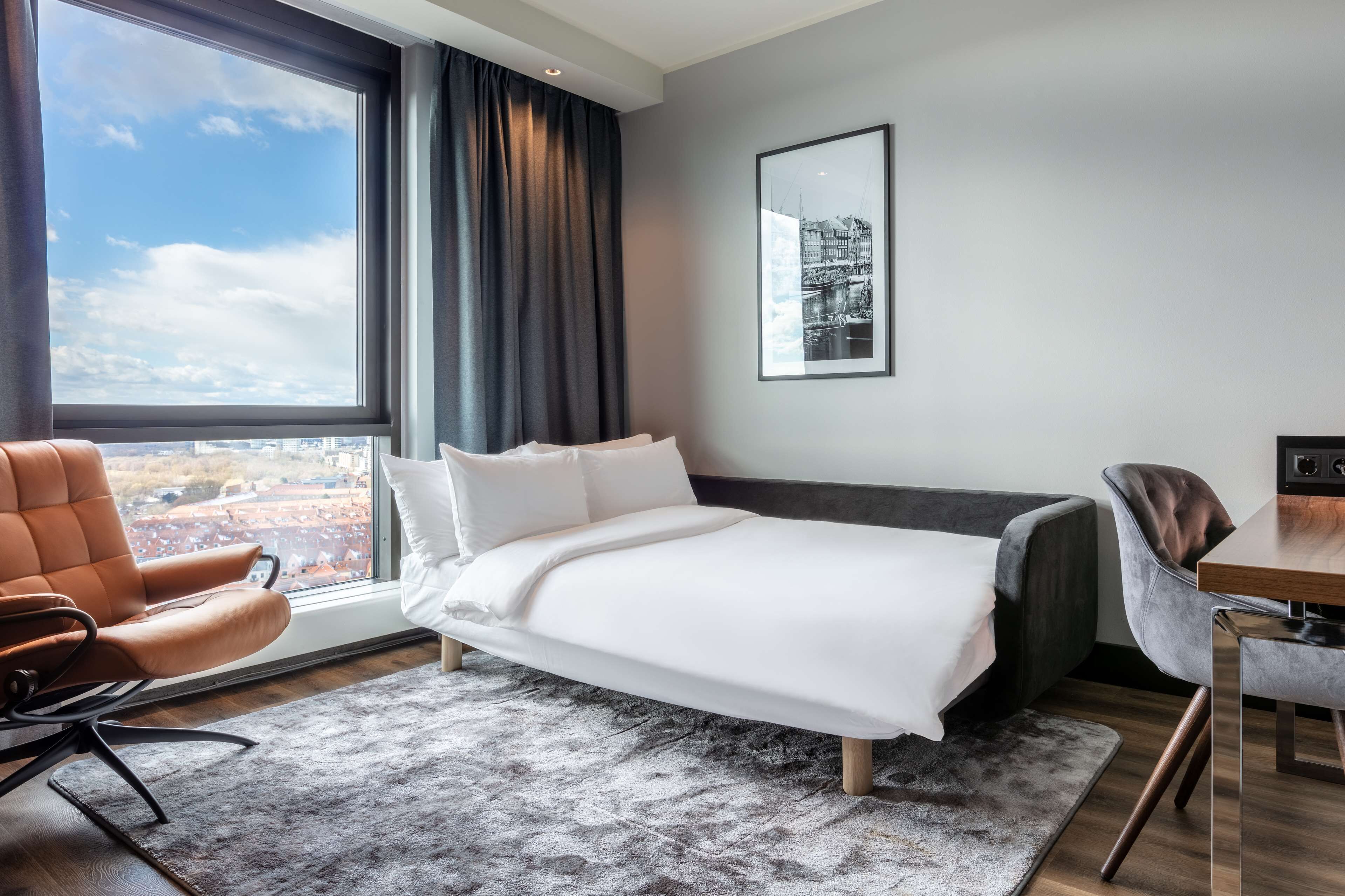 Et moderne hotelværelse med en stor seng, en sofa, et skrivebord og udsigt over byen.