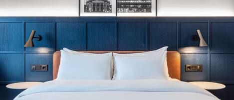 A hotel room with a large bed, two bedside tables, a headboard with built-in lighting, and framed pictures on the wall.