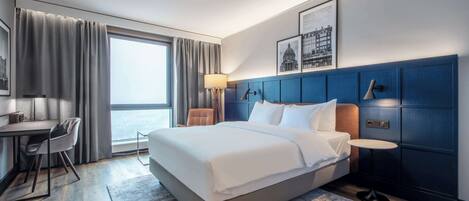 Ein modernes Hotelzimmer mit einem großen Bett, einem Schreibtisch und Blick auf die Stadt.