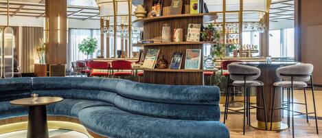 A modern lounge area with a curved blue sofa, a round table, and a bar with stools.